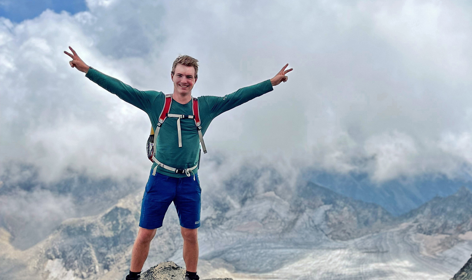 Emil steht auf einer Klippe vor einem Gletscher. Am Himmel sind große, nierige Quellwolken.