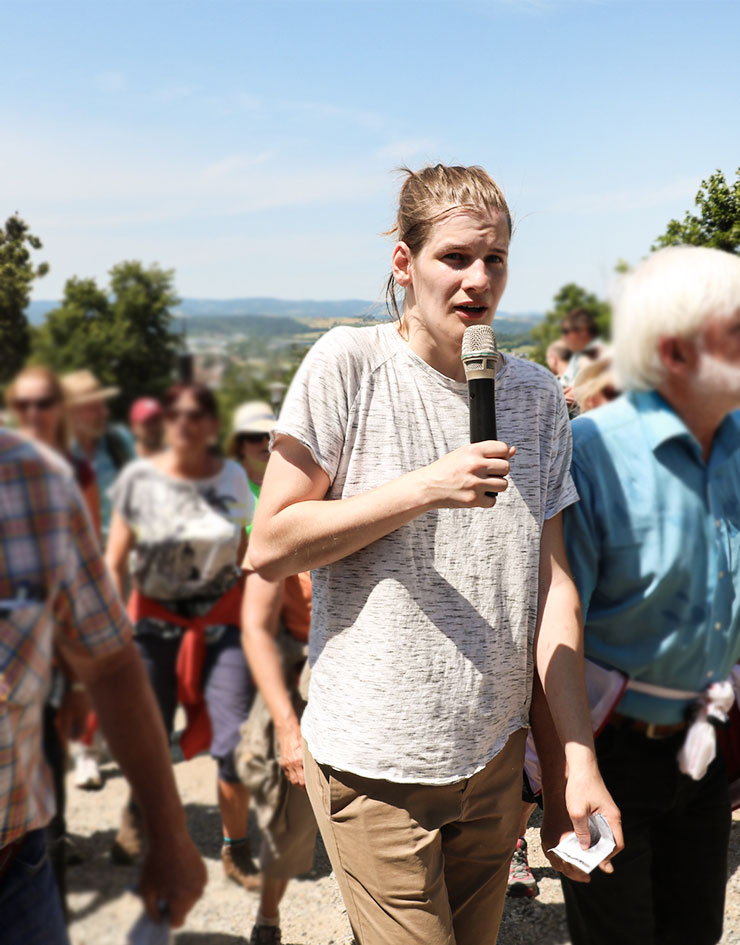 Junger Mann mit Mikrofon geht einen Berg hinauf und spricht in ein Mikro